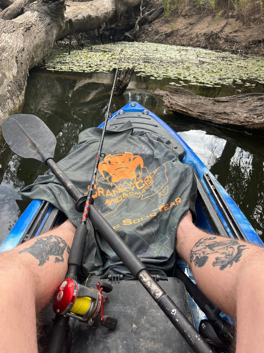 Camo fishing shirt in a kayak with a fishing rod on top of the fish shirt