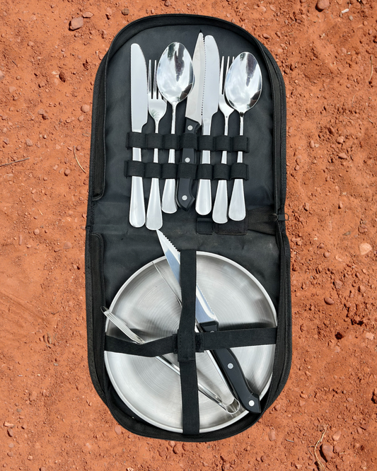 Camping Utensil Set for your camp kitchen. Utensil Set of silver cutlery and plates in a black carrying case on a red dirt background.
