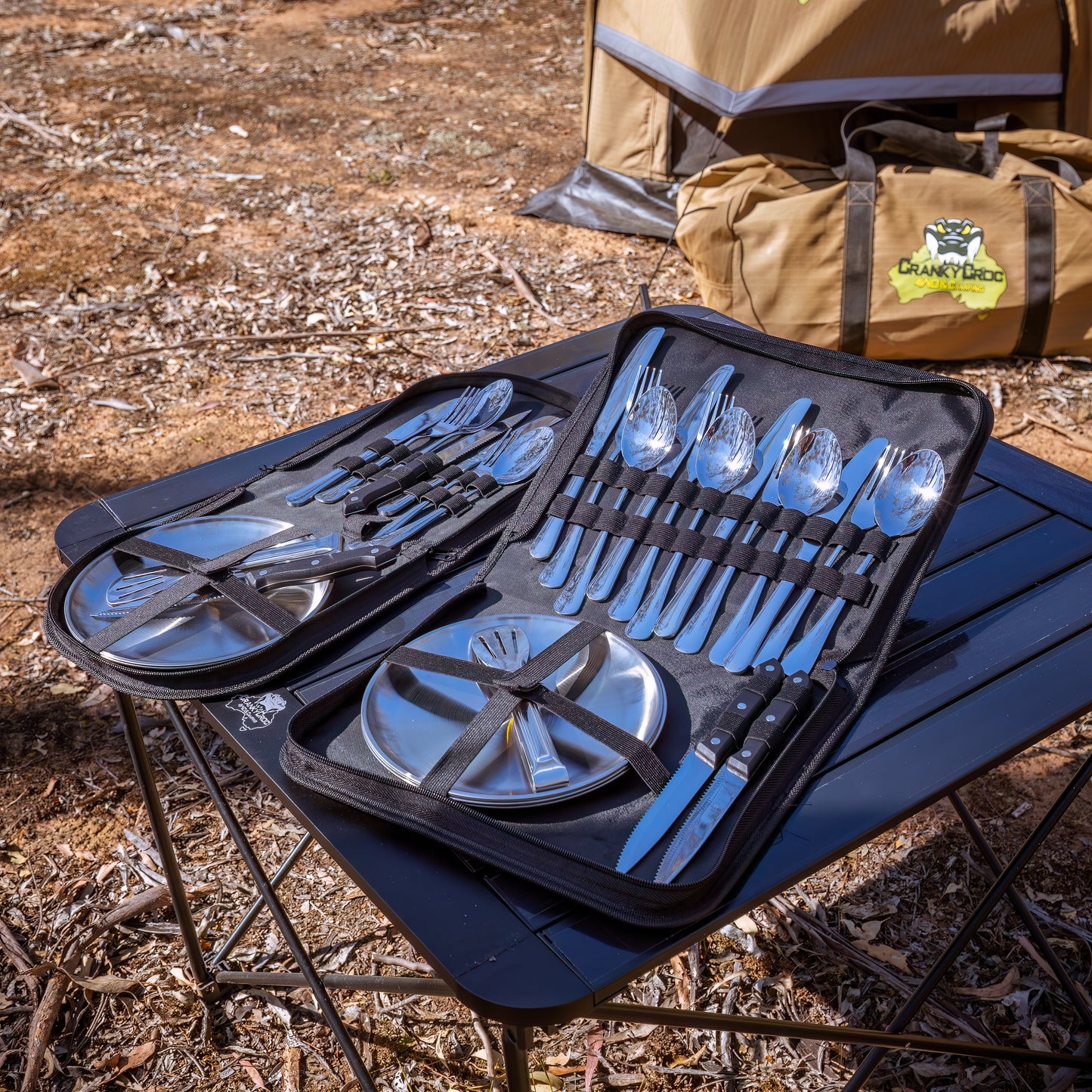 Camping Utensil Set for your camp kitchen. Utensil set of silver cutlery and plates in a black carrying case on a camping table.