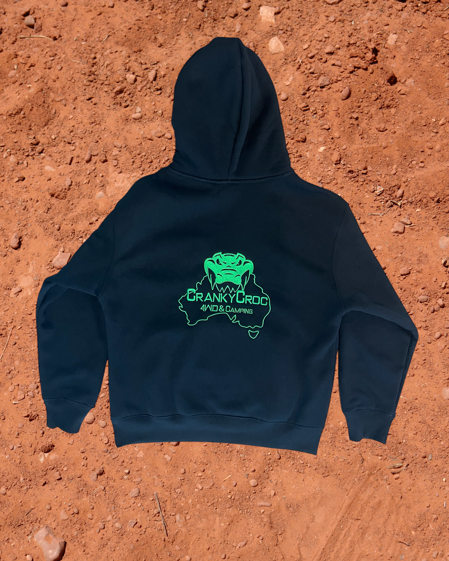back view of black hoodie with a green embroidered logo on a red dirt background