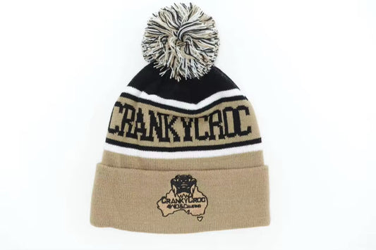 Beige warm beanie with pom-pom and 'CRANKY CROC' branding on a white background