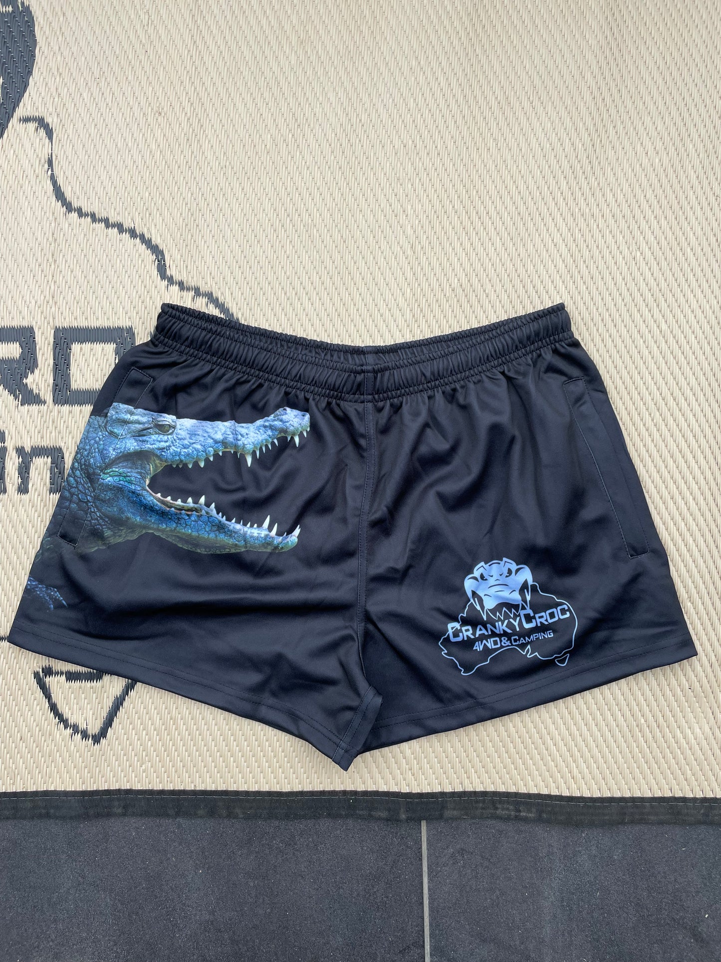 Pair of black Aussie Footy Shorts with a grey crocodile on the front. Footy Shorts with pockets