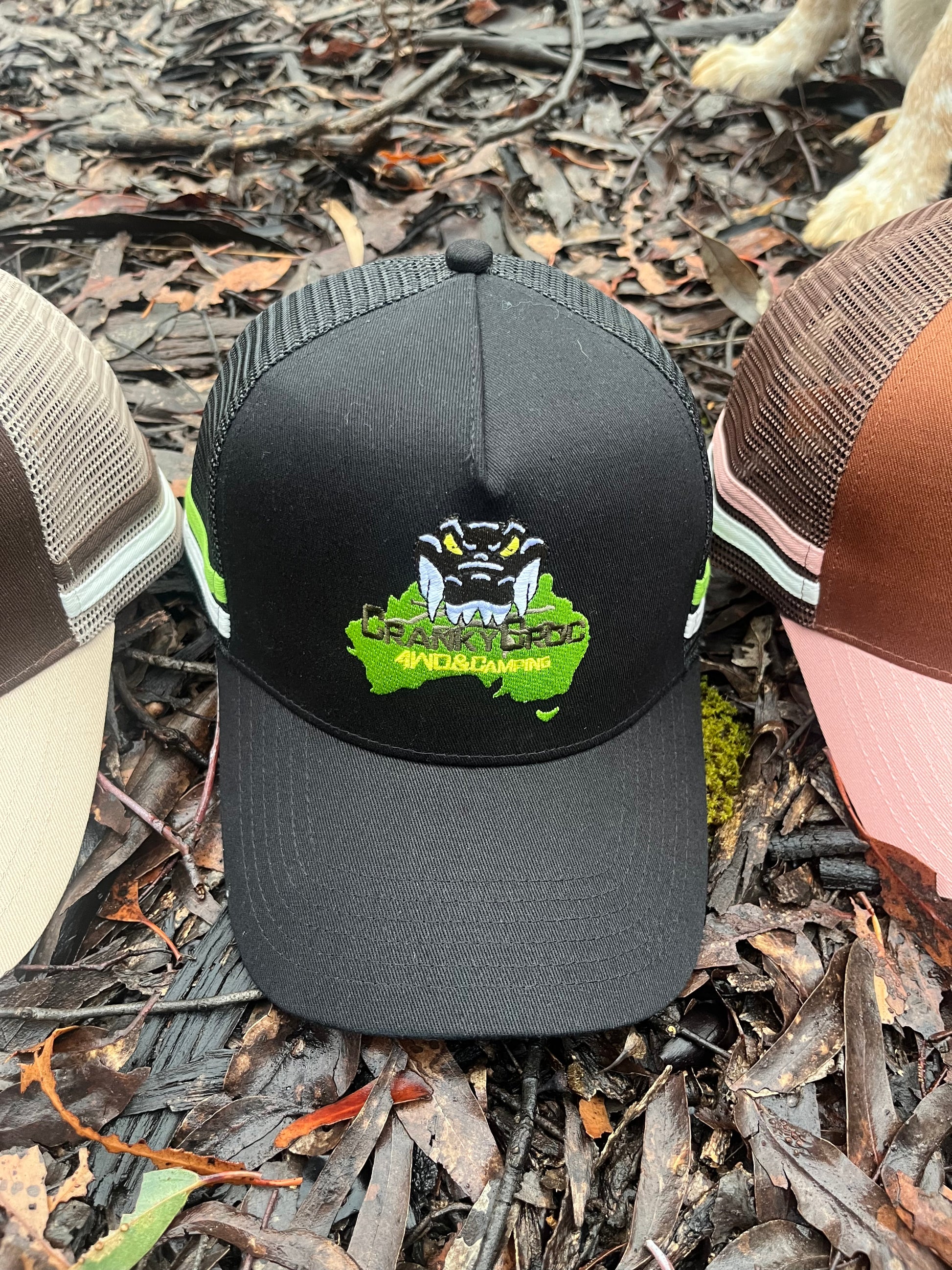 Black trucker hat with a Cranky Croc logo. The trucker cap in sitting on bark in bushland