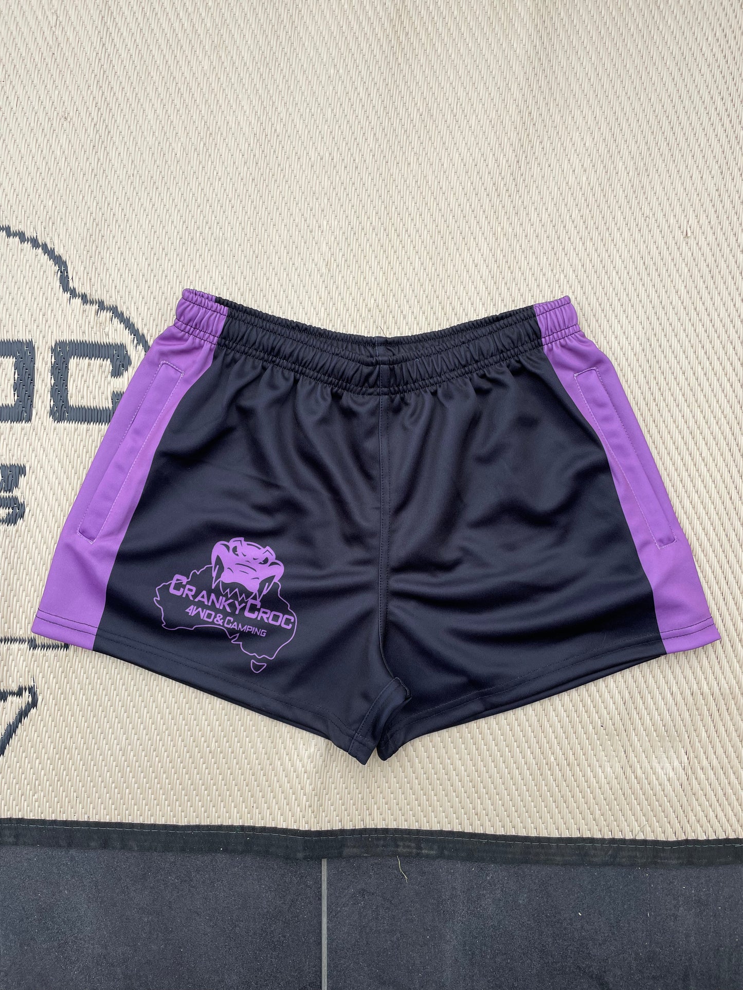 Black with purple Aussie Footy Shorts accents on a textured surface