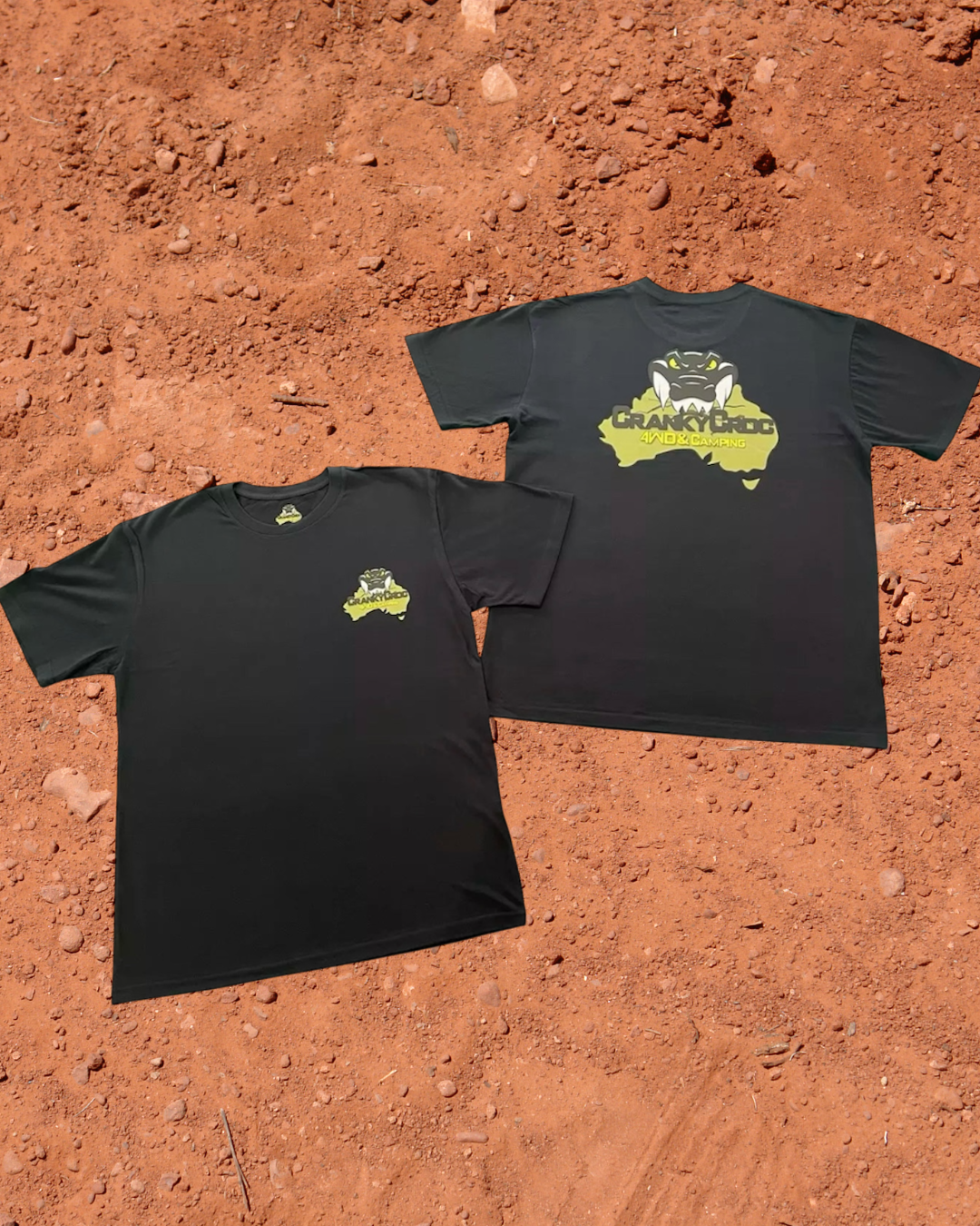 Cranky Croc branded black tees laying on a Aussie outback red dirt background. The black tees have a crocodile design