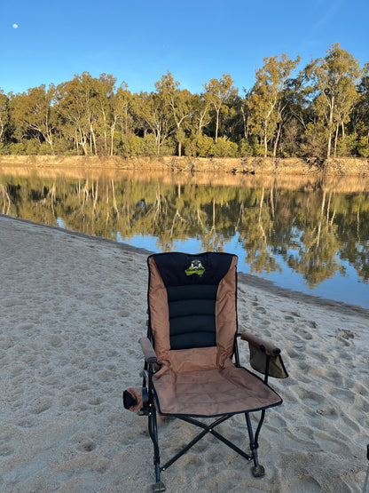 Folding chair on a sandy beach with a calm river and trees in the background