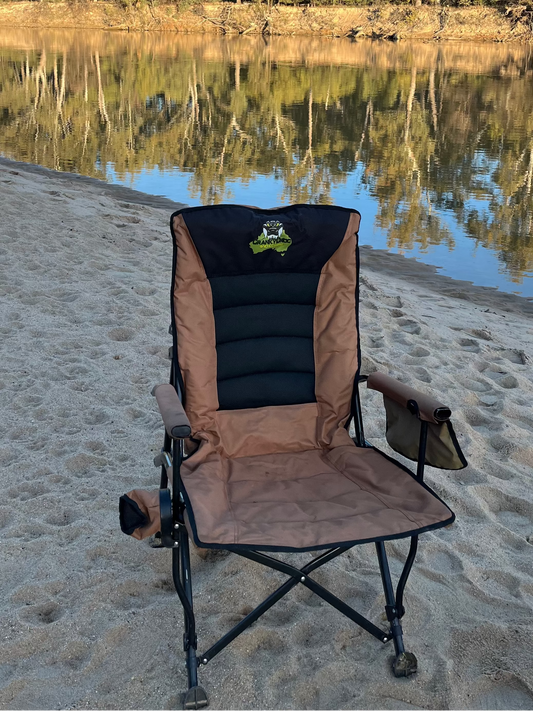 Folding chair on a sandy beach with a calm river and trees in the background