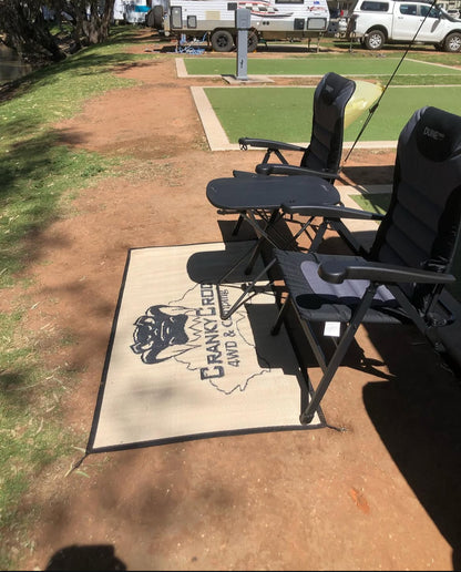 Two black reclining chairs on a camping floor mat with a logo in an outdoor camping setting.