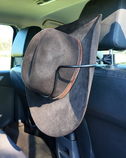 A dark brown cowboy hat with a brown band, hanging from the headrest of a car seat hat holder