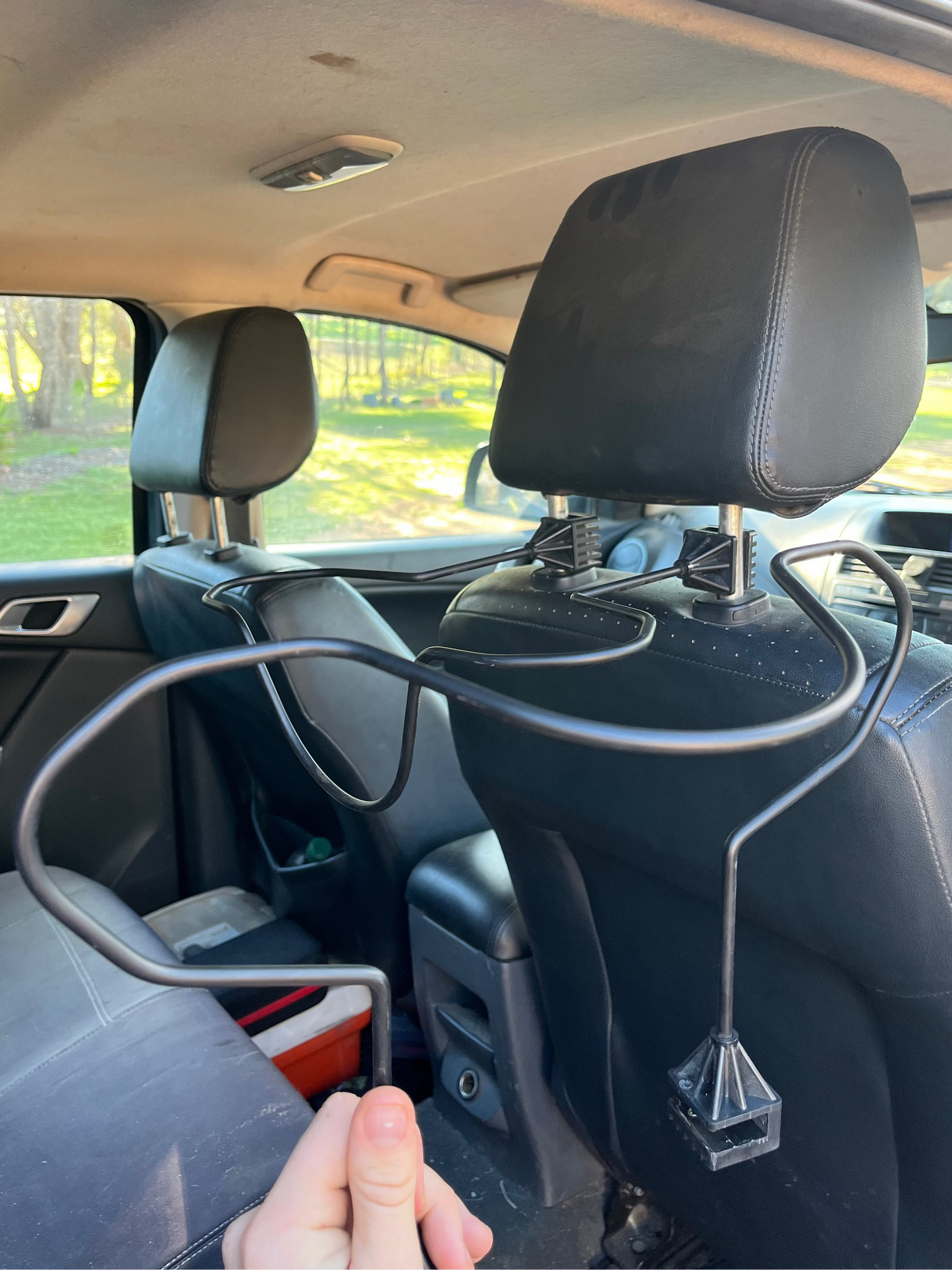 Car interior with a hand holding a Car Hat Holder which attaches to your car seat