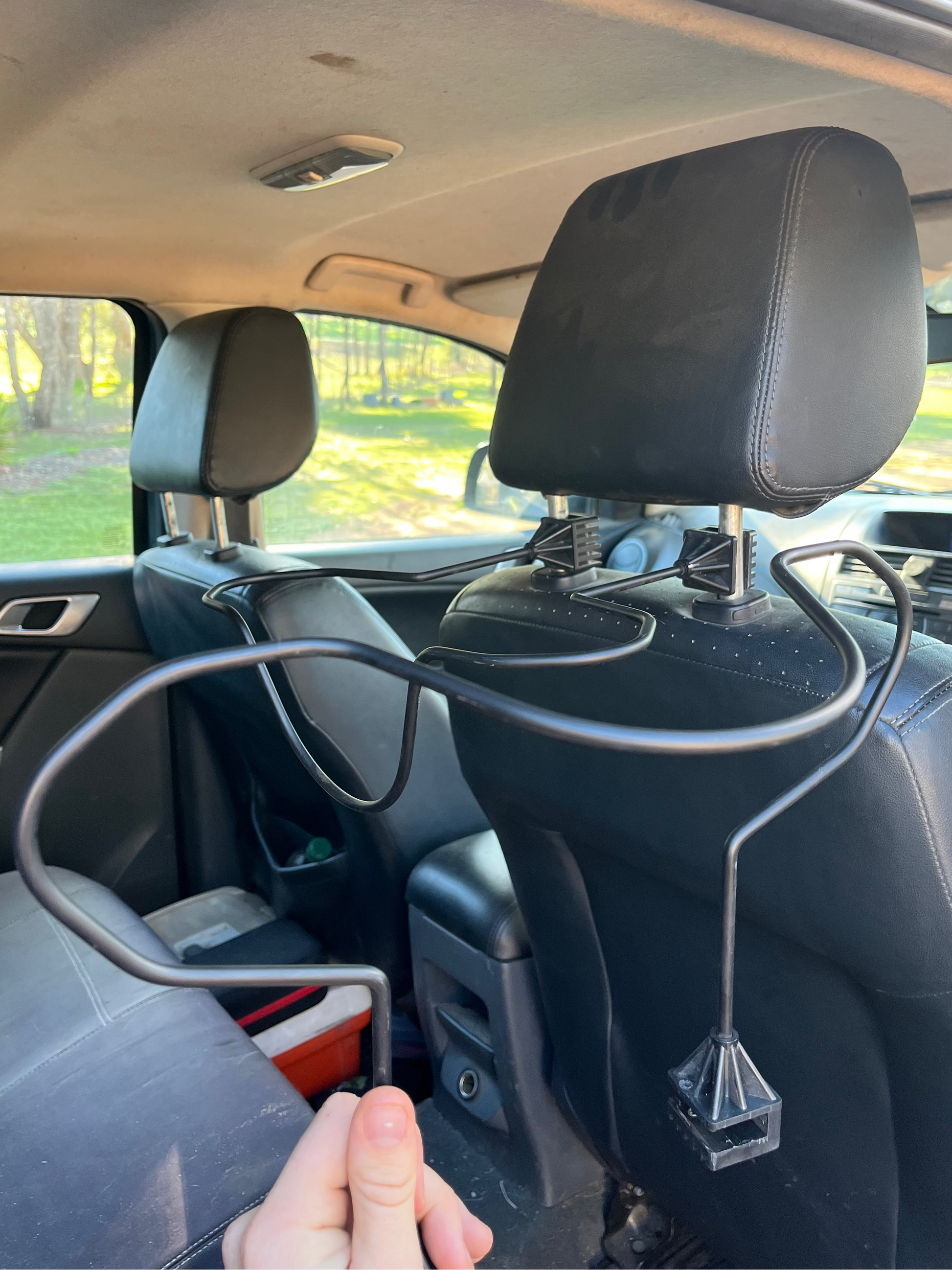 Car interior with a hand holding a Car Hat Holder which attaches to your car seat