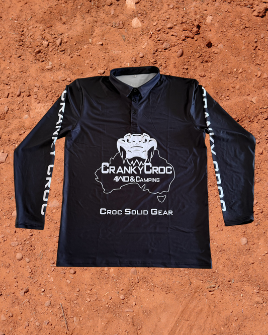 Front of black long sleeve fishing shirt, the fish shirt has white text on the sleeve with white Cranky Croc branding on the front. The logo is a crocodile biting down on Australia. Shirt is on a red dirt background