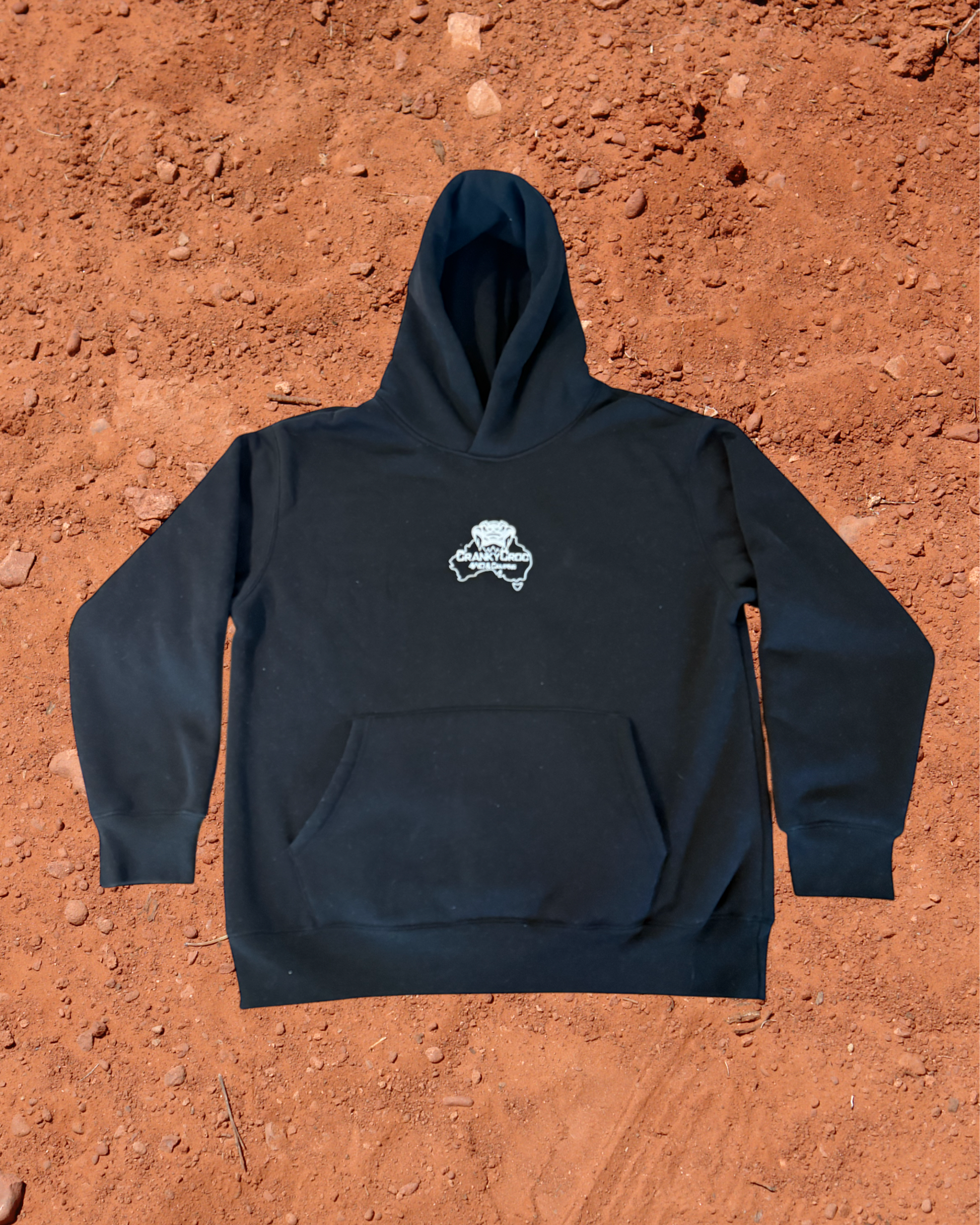 Front view of black hoodie with a white embroidered Cranky Croc logo on a red dirt background