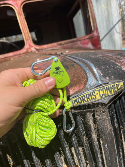 Hand holding green Cranky Croc branded tie down straps. The man is holding the ratchet straps in front of an old red Morris vehicle
