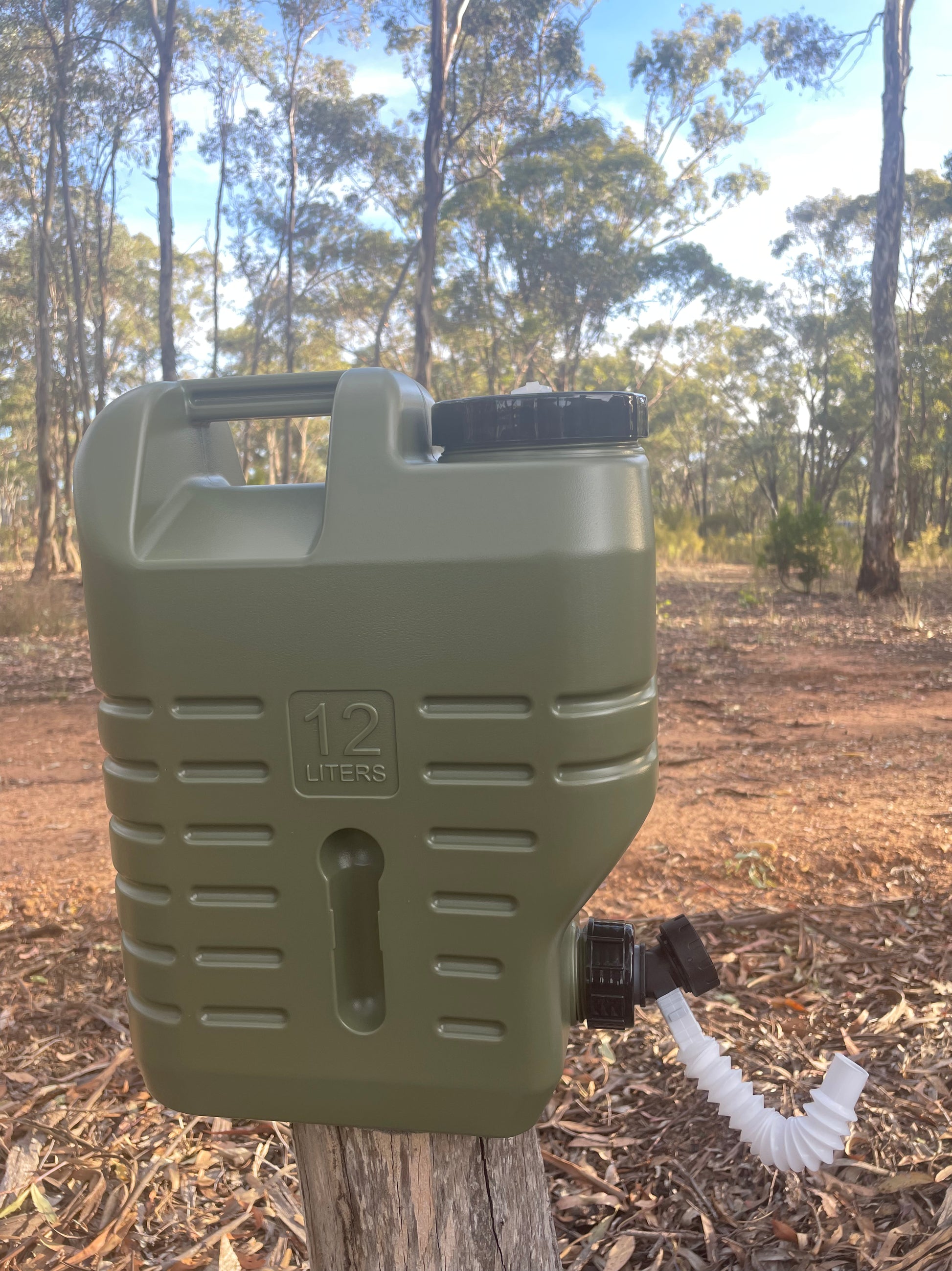 Water storage drum for camping with spout sitting on log