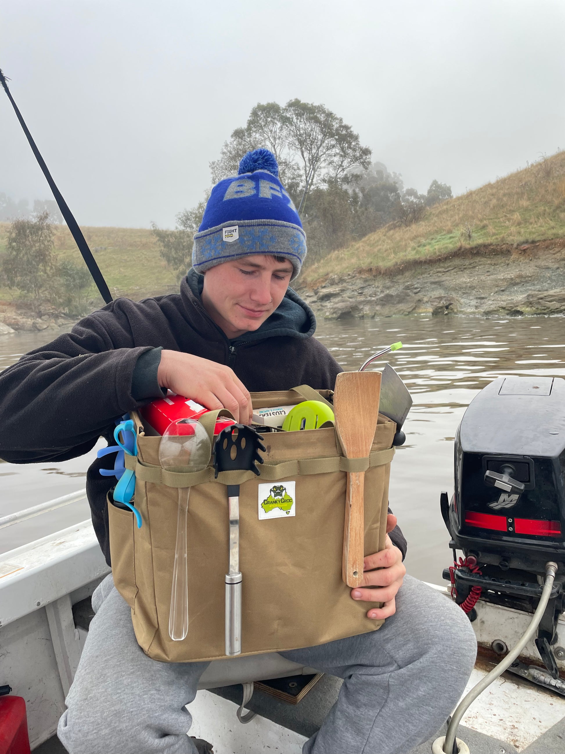 Young man sitting in fishing boat holding a Outdoor Collapsible Hamper.