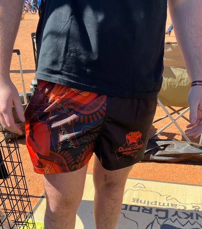 Person wearing indigenous Crocodile Footy Shorts with a logo on a dirt ground