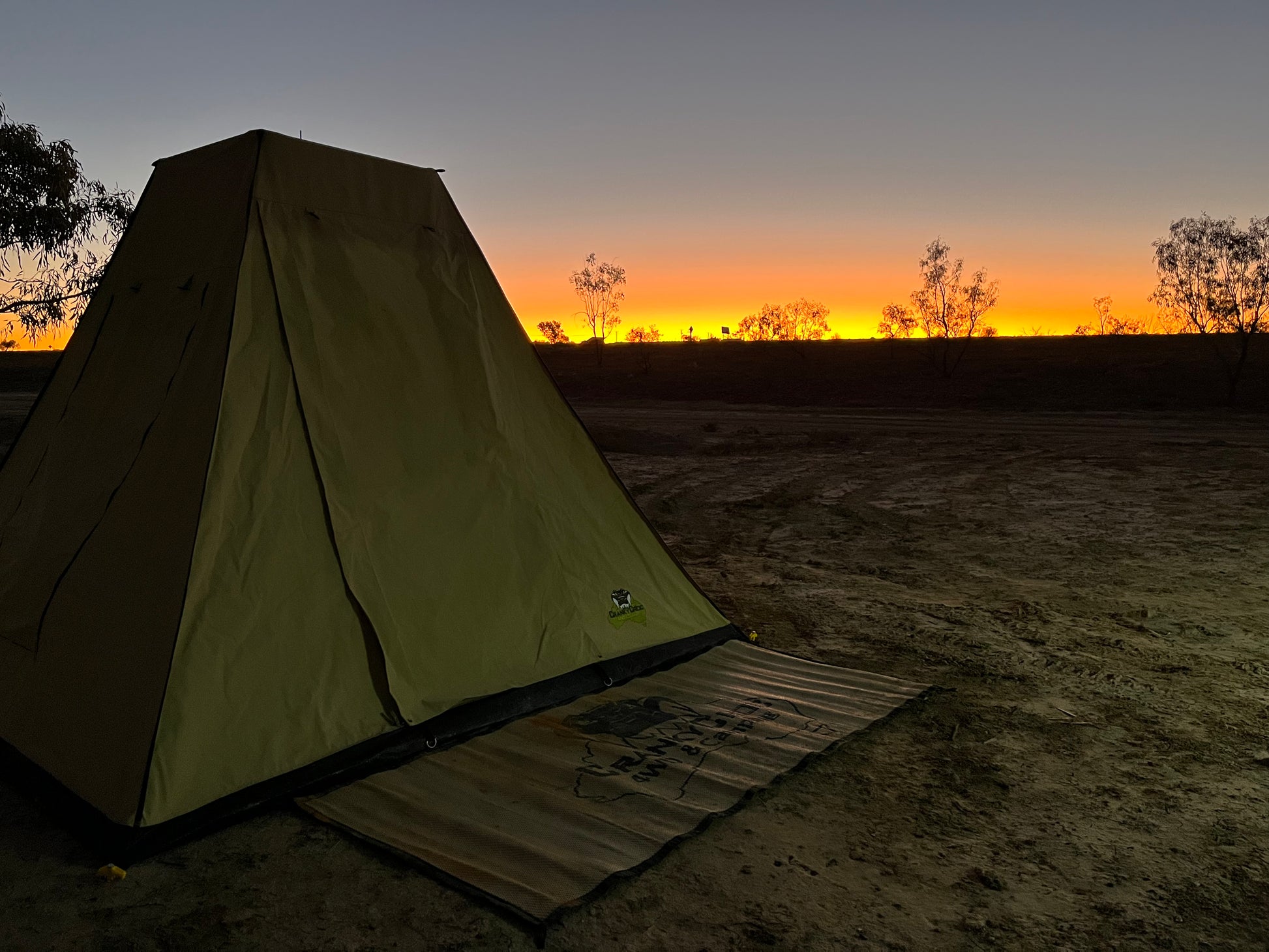 Family tent and mat on a sandy ground with a sunset sky in he outback. 