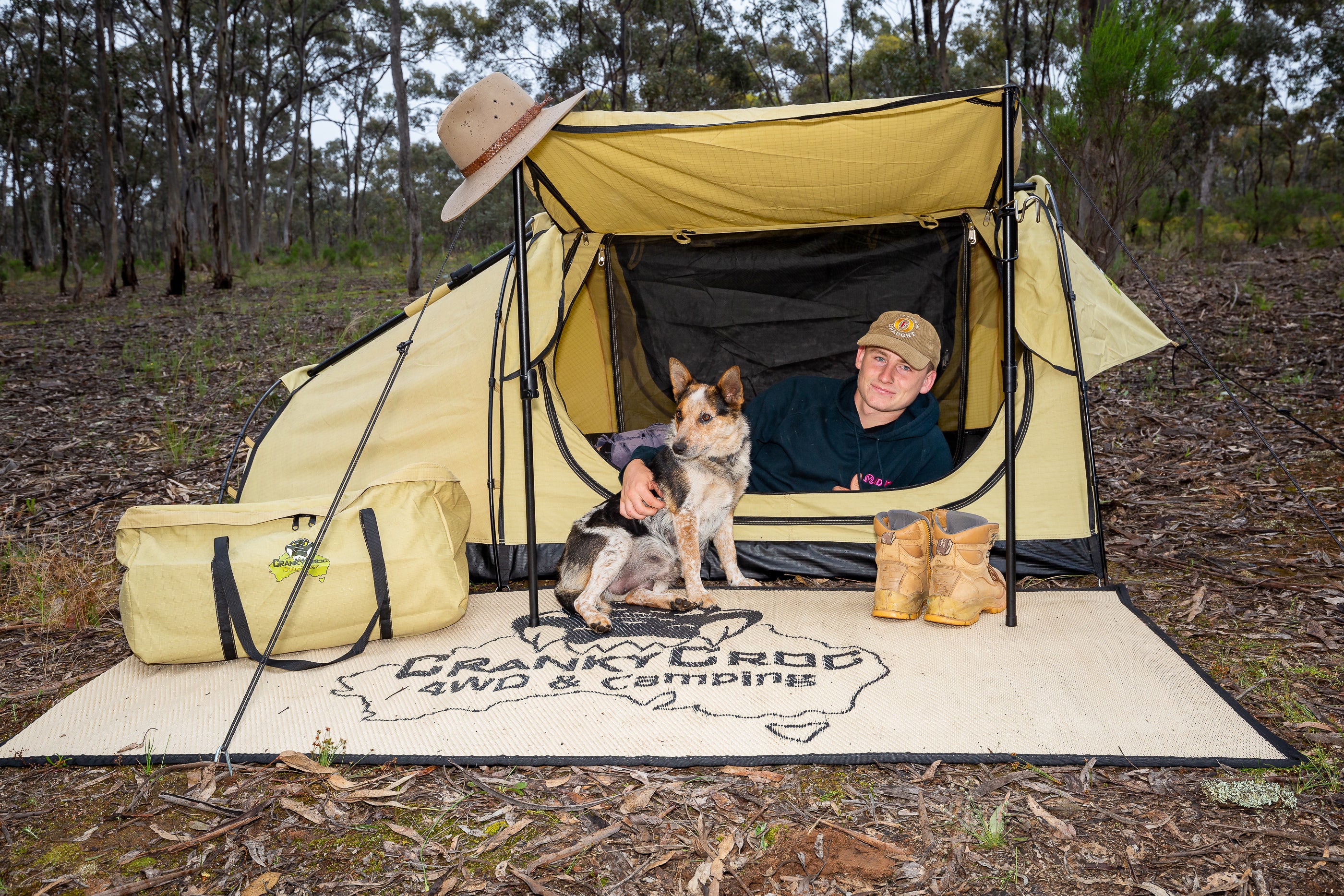 Man lying in King Single Deluxe Swag with his dog in bushland