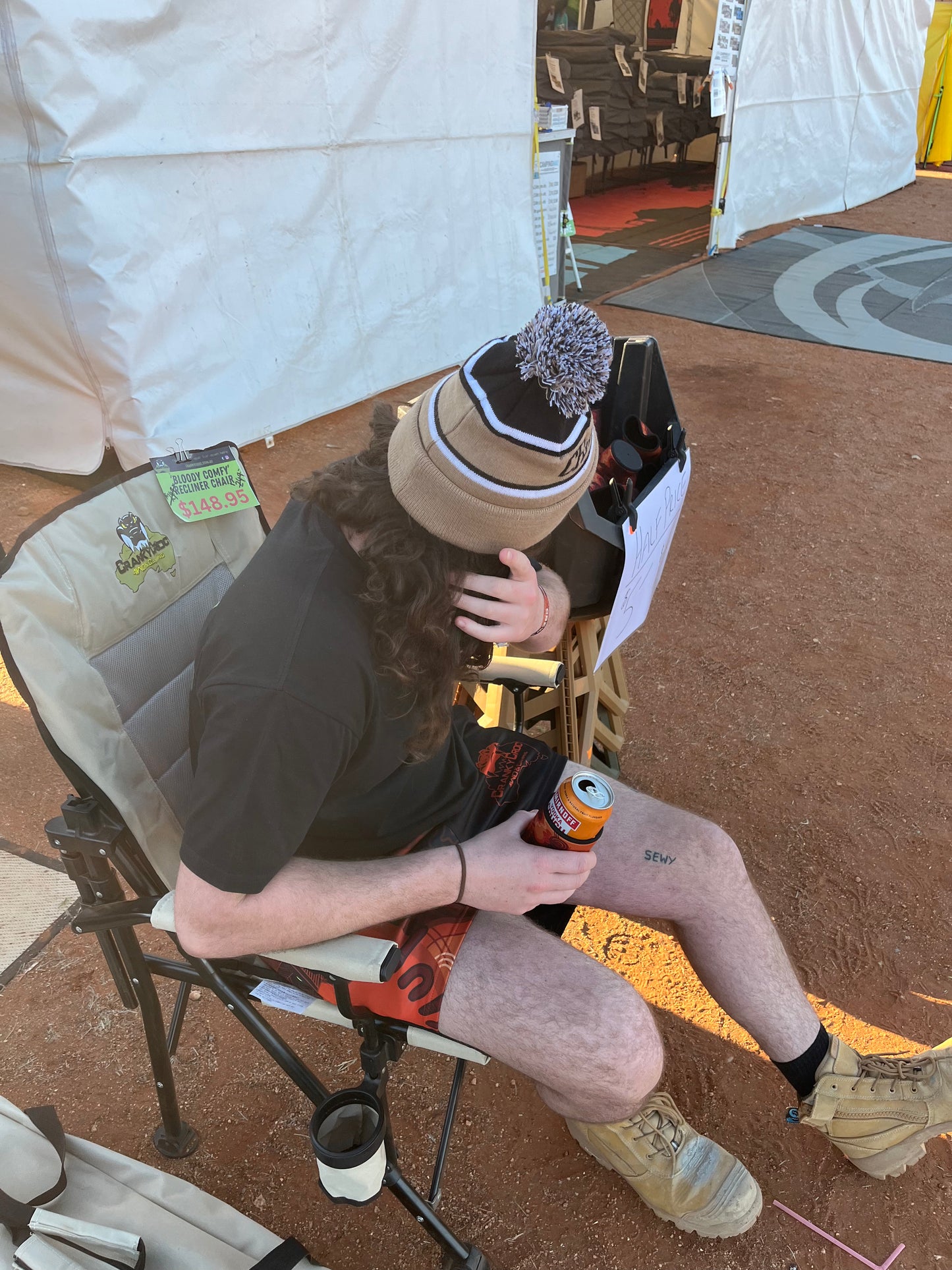 Person sitting in a camp chair with a can of beer, wearing a Beige Warm Beanie, in an outdoor setting.