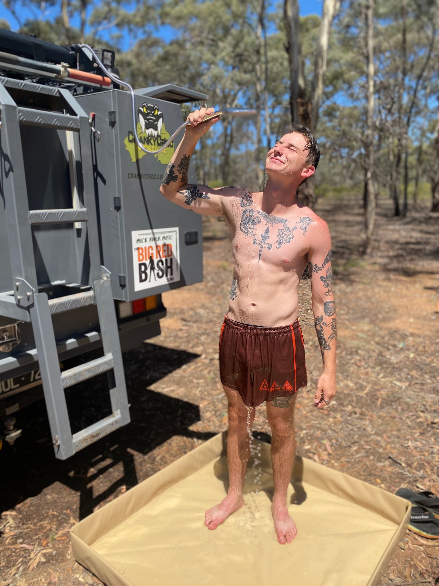 Man using his rooftop camping shower and his cranky croc shower base in bushland.