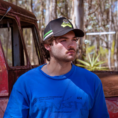 Man wearing a black trucker cap with a logo, standing in front of an old red truck.