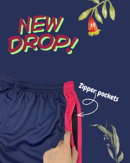 Navy blue Aussie Footy Shorts with pink sides and zipper pocket on a dark blue background with 'NEW DROP!' text and leaf graphics.