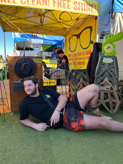 Person wearing Aussie Footy Shorts lying on the ground in front of a promotional stand with cleaning products for glasses.