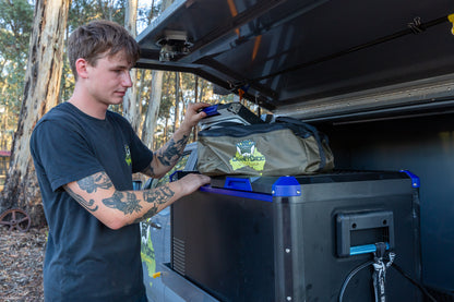 Young man standing next to a car fridge with a Mesh Top Fridge Bag sitting on top of the fridge