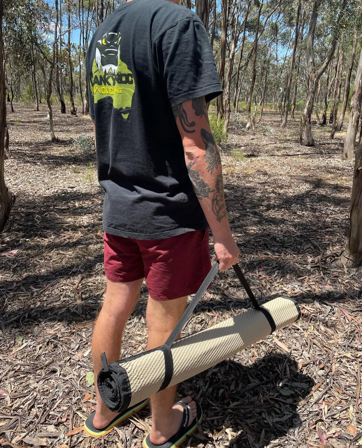 Person in bushland holding a rolled-up swag mat in bushland