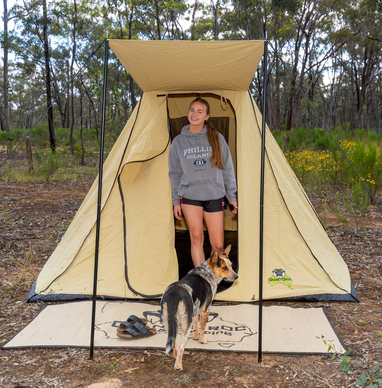 Girl standing inside tent with a camping floor mat setup in front of tent door way with dog.