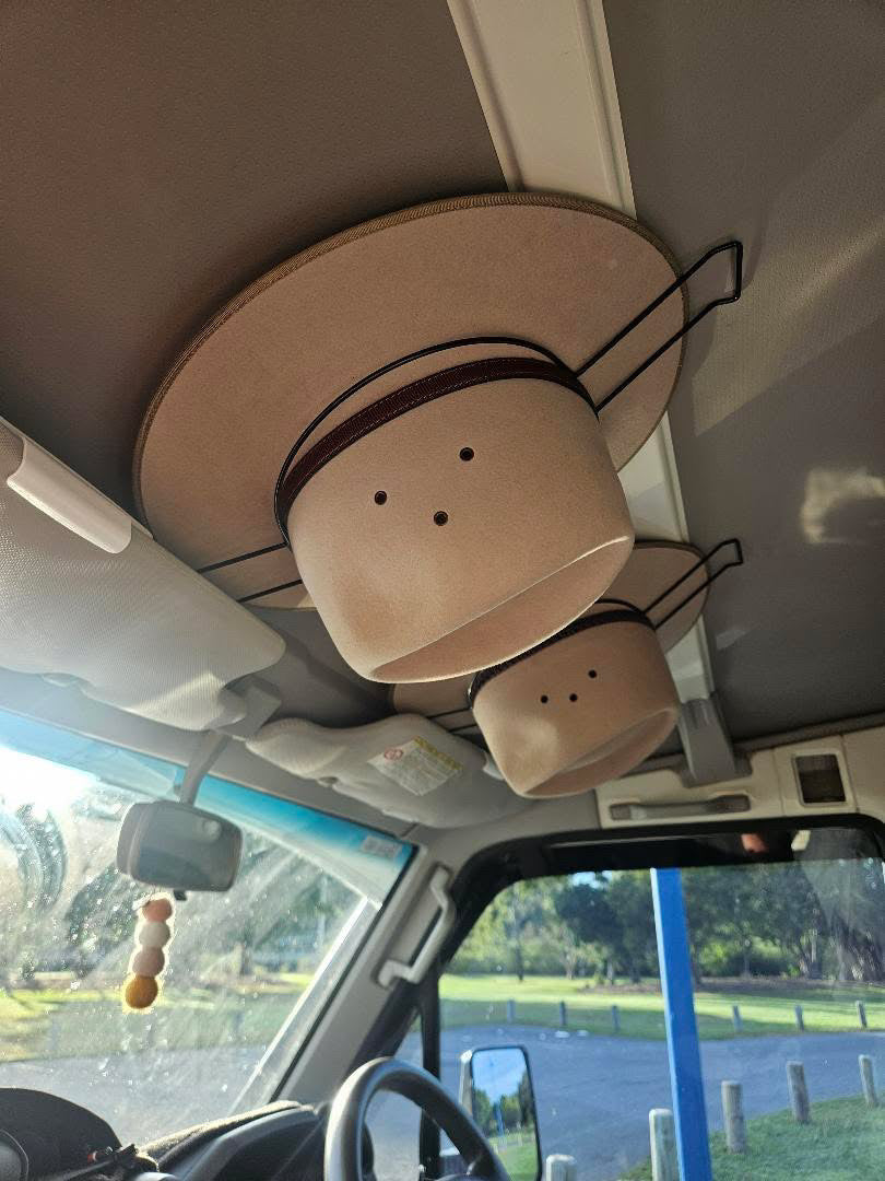 Two cowboy hats in Cranky Croc Car Hat Holder from a vehicle's sun visor with a scenic background outside.