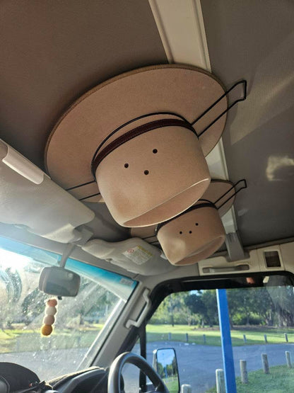 Two cowboy hats in Cranky Croc Car Hat Holder from a vehicle's sun visor with a scenic background outside.