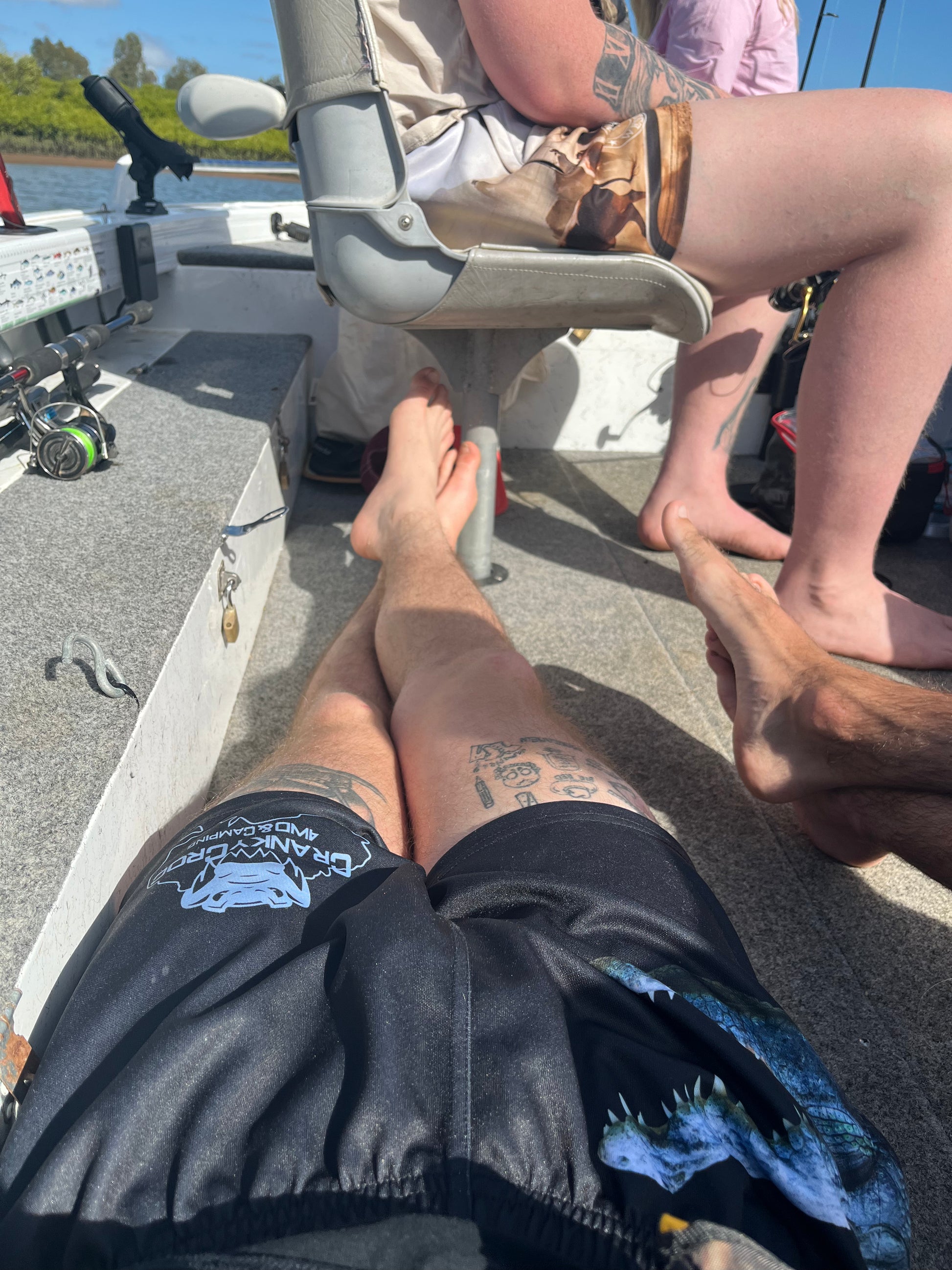 Two people sitting on a boat with feet visible, wearing black Aussie Footy Shorts.