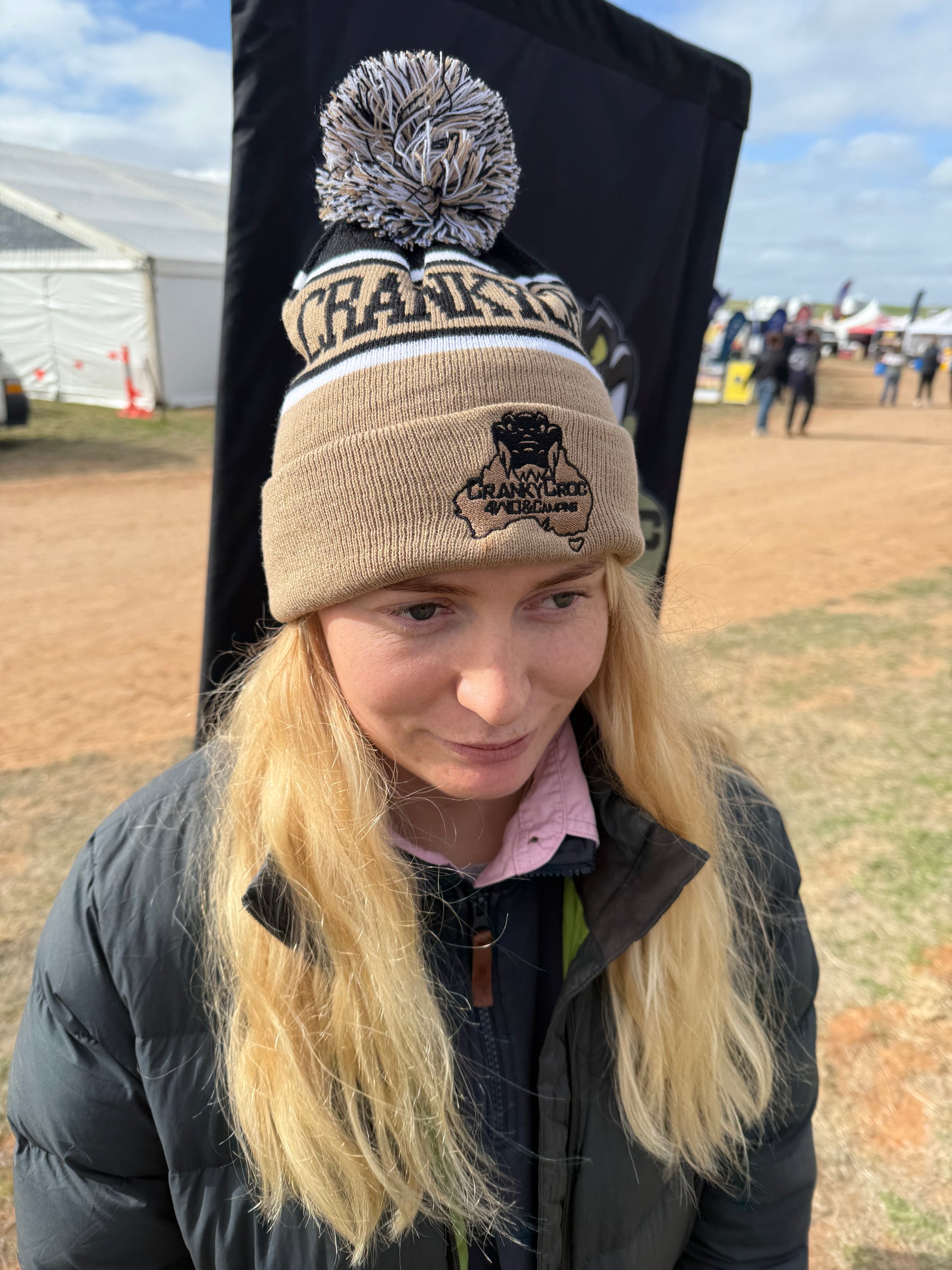 Woman wearing a beige warm beanie with a pom pom and Cranky Croc logo in an outdoor setting