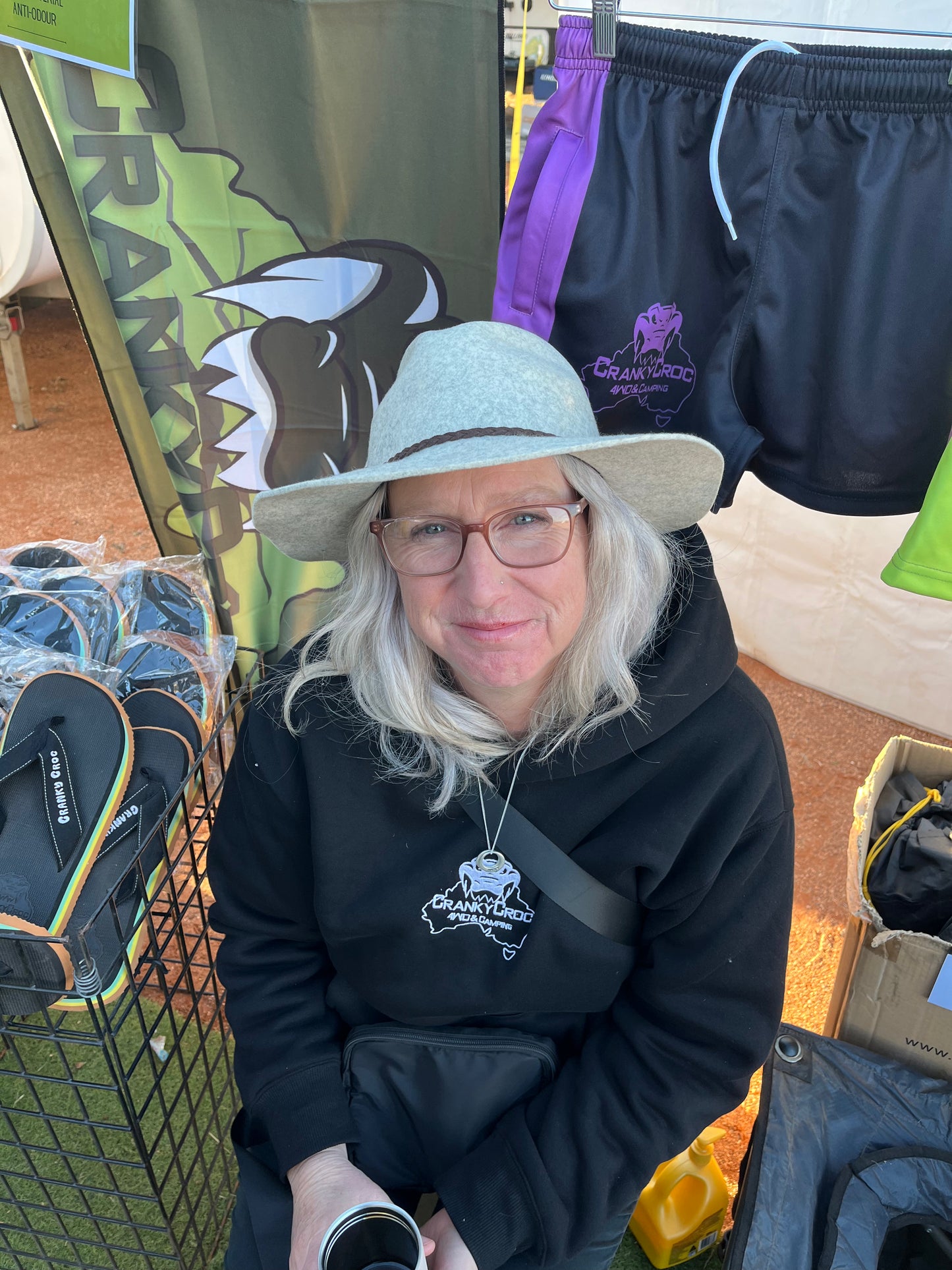 Woman wearing a black hoodie with a logo, sitting among outdoor gear and clothing.